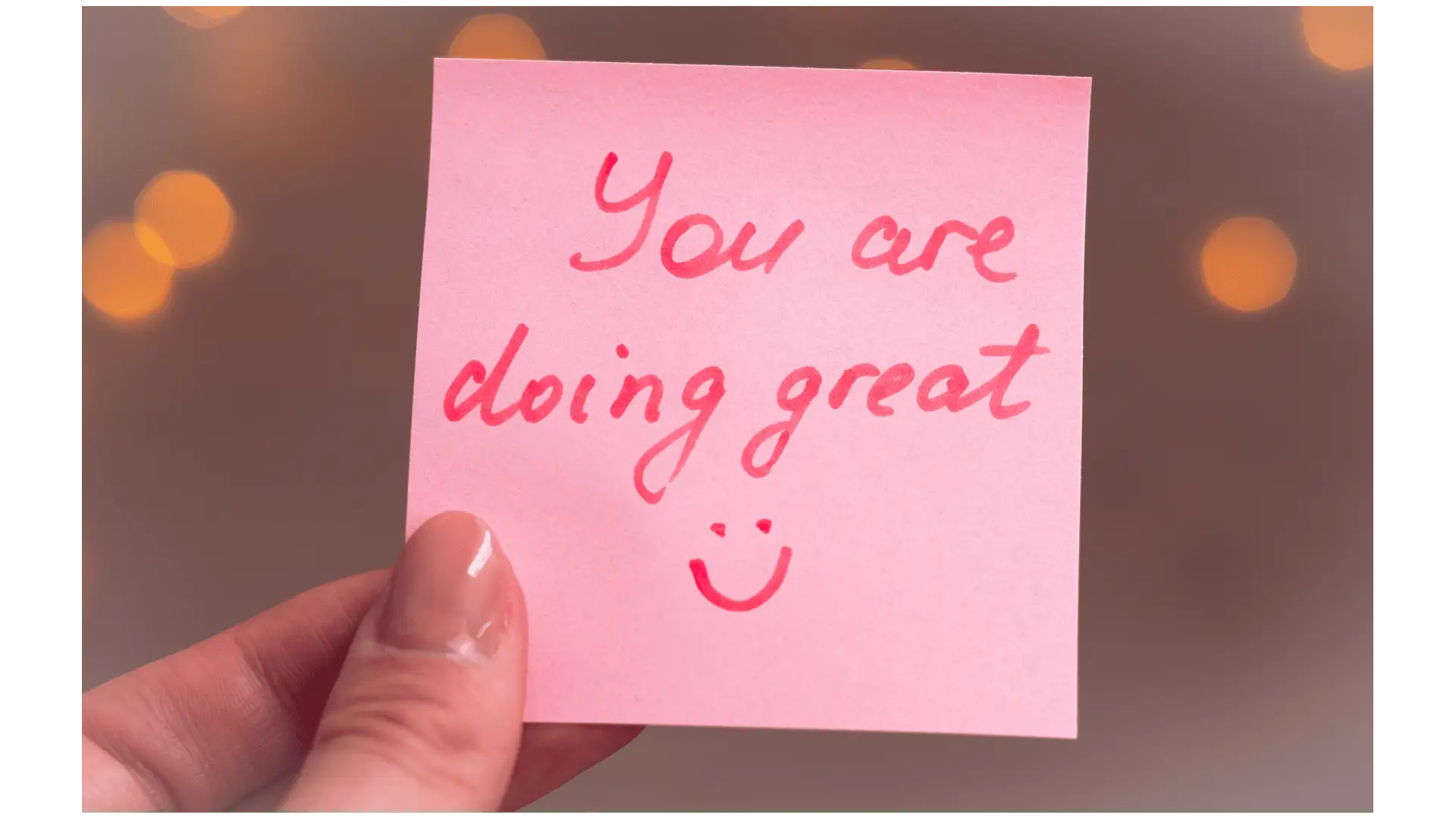 A close-up of a pink sticky note with the handwritten message "You are doing great" and a small smiley face drawn underneath.